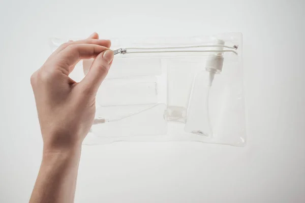 Cropped view of woman holding cosmetic bag with bottles and tube on white background — Stock Photo