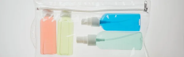 Plano panorámico de botellas de colores con líquidos en bolsa de cosméticos sobre fondo blanco - foto de stock