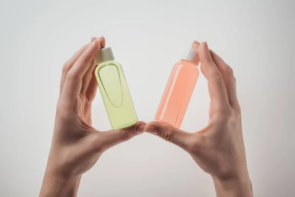 Vista recortada de la mujer sosteniendo botellas con líquidos sobre fondo blanco - foto de stock