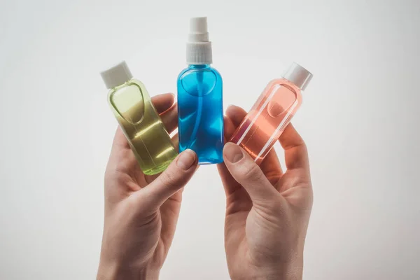 Vista recortada de la mujer sosteniendo botellas con líquidos sobre fondo blanco - foto de stock