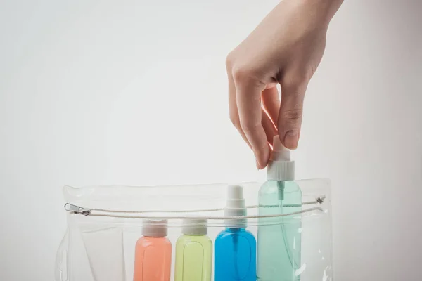 Vue recadrée de la femme mettant bouteille avec du liquide pour sac cosmétique sur fond blanc — Photo de stock