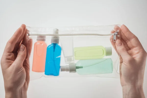 Vista recortada de la mujer sosteniendo bolsa de cosméticos con botellas de colores con líquidos sobre fondo blanco - foto de stock