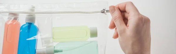 Panoramic shot of woman holding cosmetic bag with colorful bottles with liquids on white background — Stock Photo