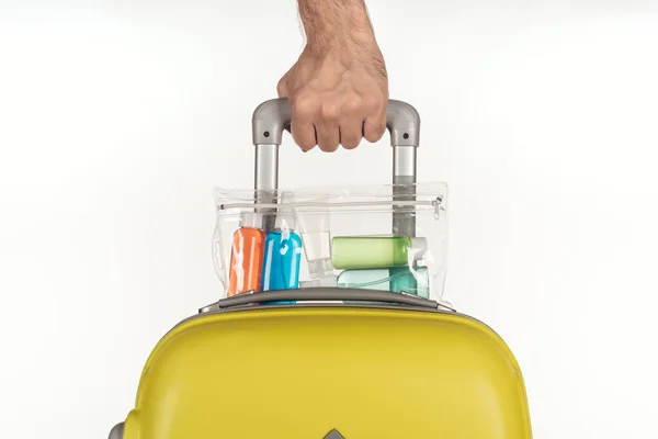 Vue recadrée de l'homme tenant sac de voyage avec sac cosmétique avec des bouteilles colorées avec des liquides sur fond blanc — Photo de stock