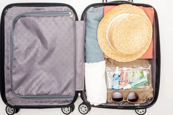 Vista dall'alto della borsa da viaggio con asciugamano, borsa cosmetica con bottiglie, vestiti, occhiali da sole e cappello su sfondo bianco — Foto stock