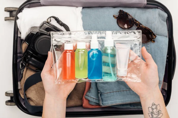 Abgeschnittene Ansicht einer Frau, die Reisetasche mit Kosmetiktasche mit bunten Flaschen verpackt — Stockfoto