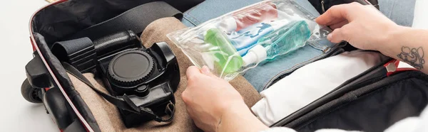 Vista recortada de la mujer embalaje bolsa de viaje con bolsa de cosméticos con botellas de colores - foto de stock