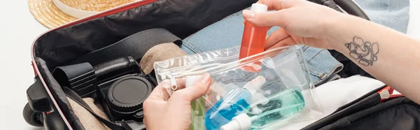 Panoramic shot of woman packing travel bag with cosmetic bag with colorful bottles — Stock Photo