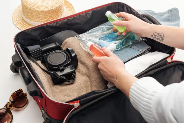 Vista recortada de la mujer embalaje bolsa de viaje con bolsa de cosméticos con botellas de colores - foto de stock