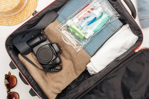 Vista dall'alto della borsa da viaggio con asciugamano, borsa cosmetica con bottiglie colorate, fotocamera digitale, vestiti — Foto stock