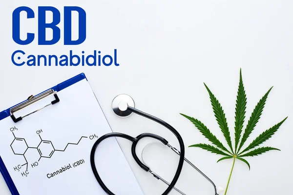 Vista dall'alto della foglia di cannabis medica, appunti con l'illustrazione della molecola cbd vicino allo stetoscopio su sfondo bianco con scritte di cannabidiolo — Foto stock