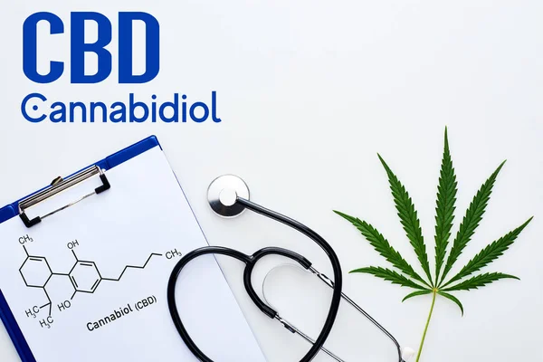 Vue du dessus de la feuille de cannabis médical, presse-papiers avec illustration de molécules de cbd près du stéthoscope sur fond blanc avec lettrage au cannabidiol — Photo de stock