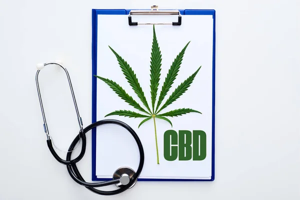 Top view of medical cannabis leaf on clipboard with cbd lettering near stethoscope on white background — Stock Photo