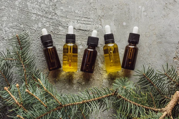 Top view of bottles with naturaloil near fir branches on grey stone surface — Stock Photo