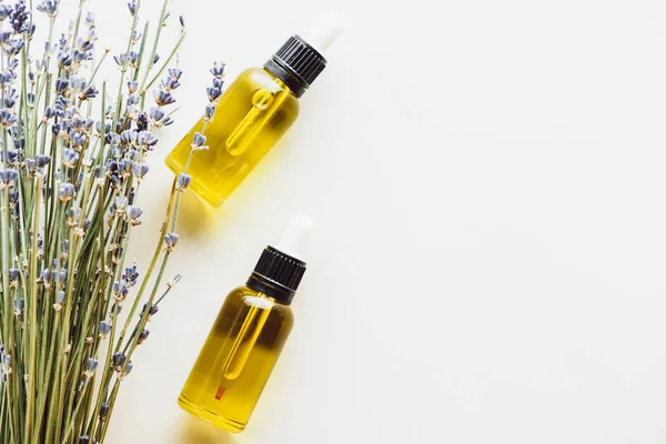 Draufsicht auf trockene Lavendelzweige mit Blumen und Flaschen mit natürlichem Öl auf weißem Hintergrund mit Kopierraum — Stockfoto