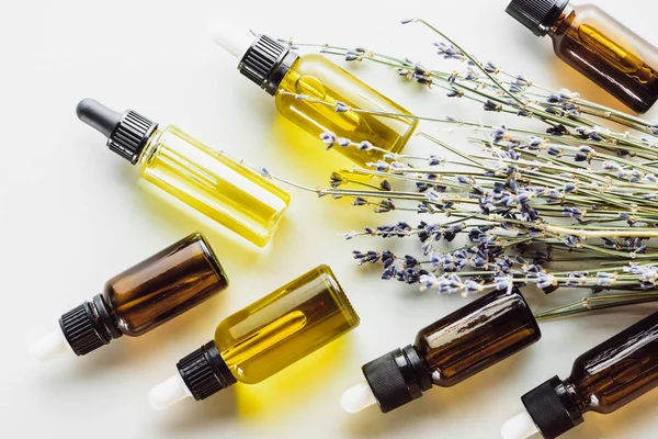 Vue de dessus des brindilles de lavande sèches avec des fleurs et des bouteilles avec de l'huile naturelle sur fond blanc — Photo de stock