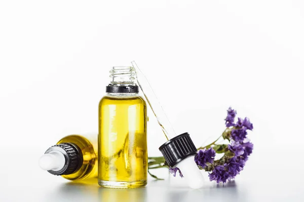 Botellas de aceite natural y ramita de limonio seco con flores aisladas en blanco - foto de stock