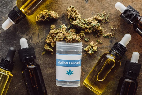 Вид зверху на медичні марихуани поблизу контейнера і пляшки з конопляною олією на мармуровій поверхні — стокове фото