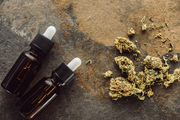 Vue de dessus des bourgeons de marijuana médicale près des bouteilles avec de l'huile de chanvre sur la surface du marbre — Photo de stock