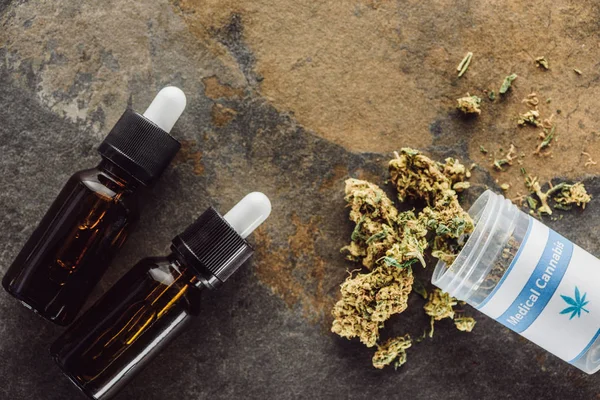 Vista superior de brotes de marihuana medicinal cerca de contenedor y botellas con aceite de cáñamo en la superficie de mármol - foto de stock