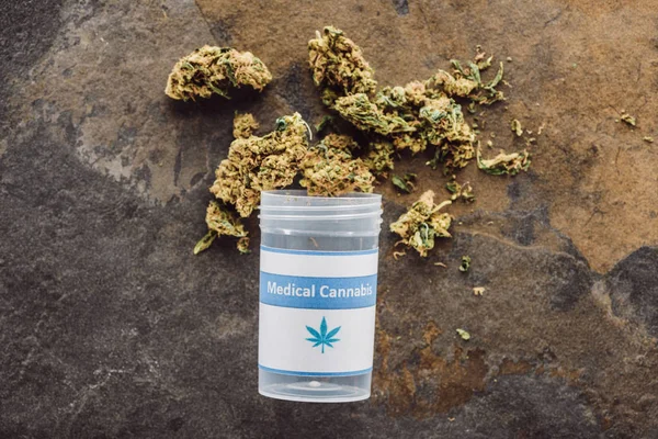 Top view of medical marijuana buds near container on marble surface — Stock Photo