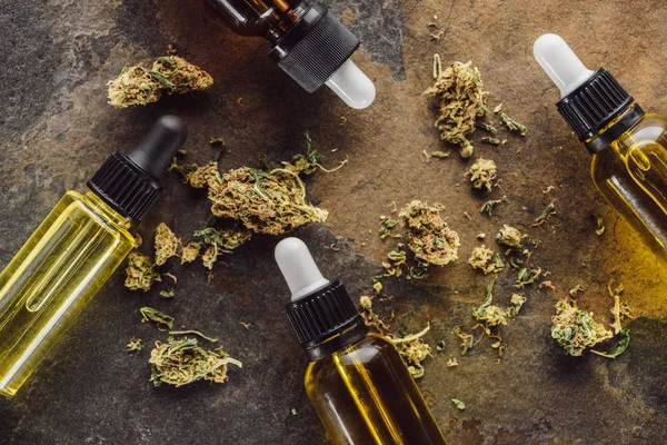 Vista superior de brotes de marihuana medicinal cerca de botellas con aceite de cáñamo en la superficie de mármol - foto de stock
