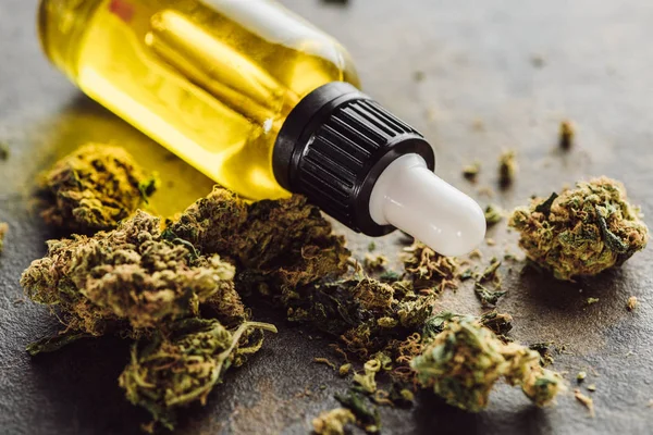 Vue rapprochée des bourgeons de marijuana médicale près de la bouteille avec de l'huile de chanvre sur la surface du marbre — Photo de stock