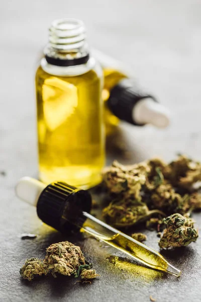 Foyer sélectif de compte-gouttes avec de l'huile de chanvre, des bourgeons de marijuana médicale et des bouteilles sur la surface de pierre — Photo de stock