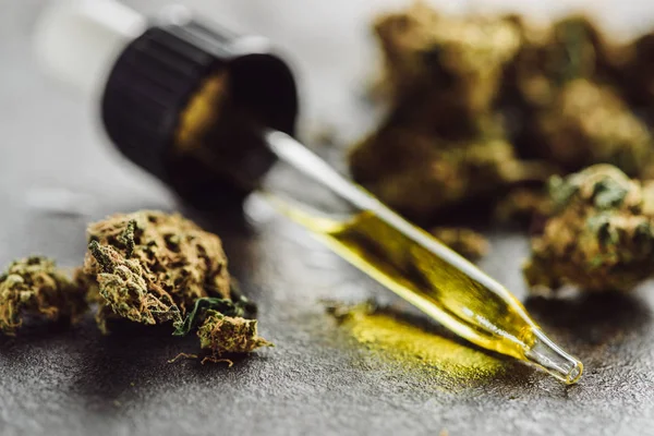 Close up view of medical marijuana buds and dropper with hemp oil on stone surface — Stock Photo