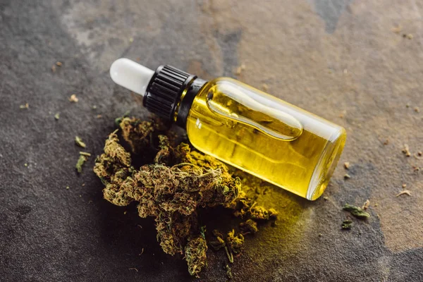 Bottle with natural oil near medicine marijuana buds on marble surface — Stock Photo