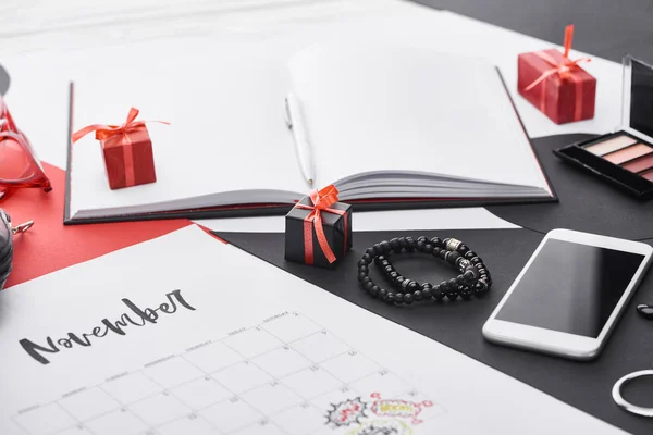 Foco seletivo do calendário com letras novembro, sombra de olhos, presentes, smartphone, notebook e pulseiras — Fotografia de Stock