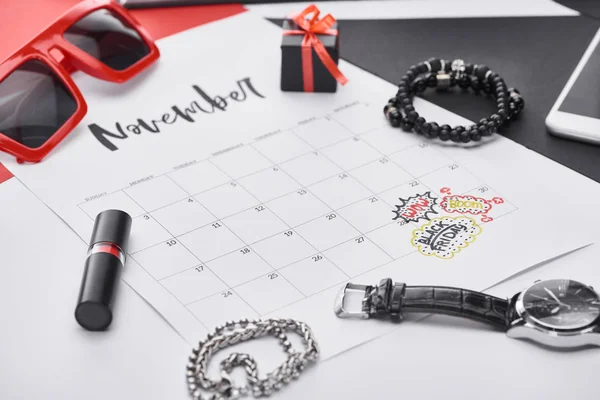 Foco seletivo do calendário com letras novembro, batom, presente, óculos de sol, pulseiras, relógio de pulso — Fotografia de Stock