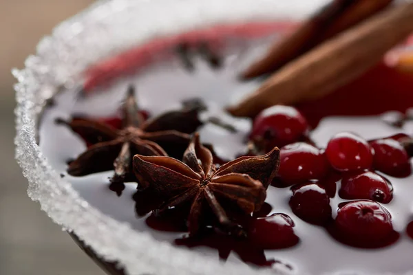 Close up view of red spiced mulled wine with berries, anise, orange slices and cinnamon in glass decorated with sugar — Stock Photo