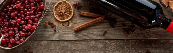 Vista superior del vino tinto en botella cerca de bayas, anís, rodajas de naranja y canela en la mesa rústica de madera, plano panorámico - foto de stock