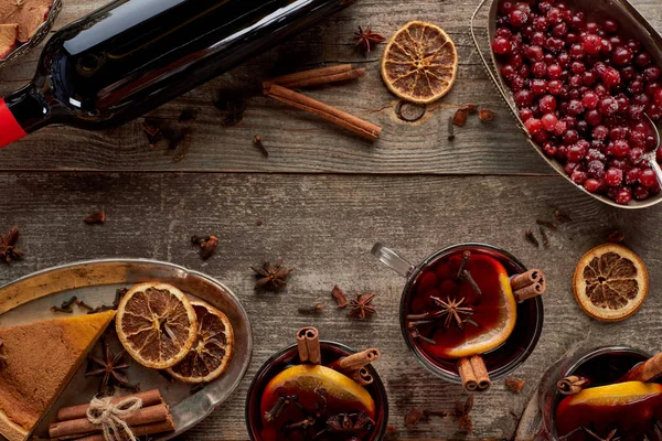 Top view of piece of pie, bottle and red spiced mulled wine with berries, anise, orange slices and cinnamon on wooden rustic table — Stock Photo