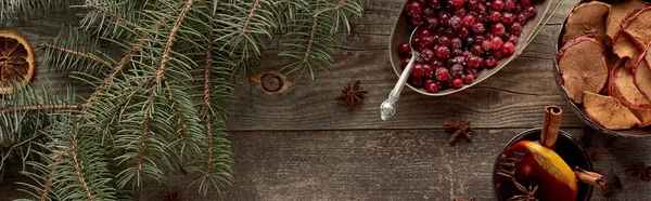 Top view of red spiced mulled wine with berries, anise, orange slices and cinnamon on wooden rustic table near fir branch, panoramic shot — Stock Photo