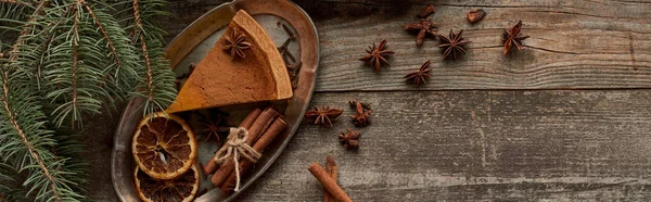 Top view of piece of pie, anise, dry orange slices and cinnamon on wooden rustic table near fir branch, panoramic shot — Stock Photo