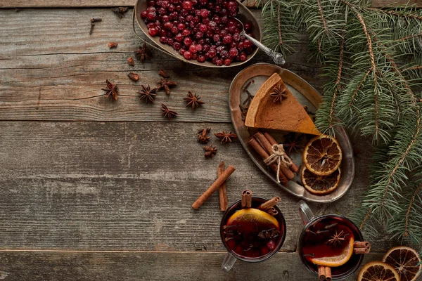 Top view of red spiced mulled wine near fir branch, pie, berries, anise, orange slices and cinnamon on wooden rustic table — Stock Photo
