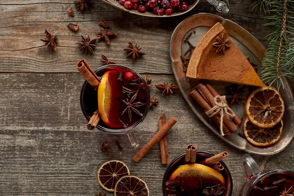 Vista superior de vinho tinto temperado mulled perto de ramo de abeto, torta, bagas, anis, fatias de laranja e canela na mesa rústica de madeira — Fotografia de Stock