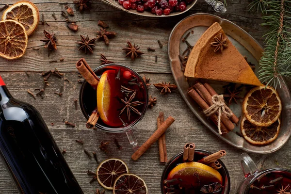 Vista superior de vinho tinto temperado mulled perto de ramo de abeto, torta, bagas, anis, fatias de laranja e canela na mesa rústica de madeira — Fotografia de Stock