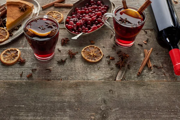 Red spiced mulled wine near bottle, piece of pie, berries, anise, orange slices and cinnamon on wooden rustic table with copy space — Stock Photo