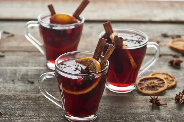 Vino caliente con especias rojas con bayas, anís, rodaja de naranja y canela en la mesa rústica de madera - foto de stock