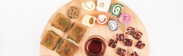 Vue du dessus de la planche de bois avec de délicieux bonbons turcs et thé isolé sur blanc, panoramique — Photo de stock