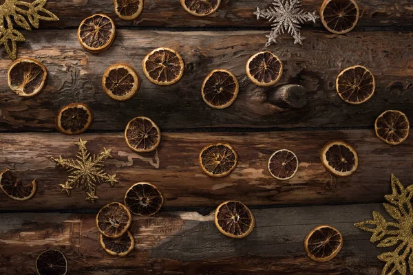 Vista superior de rodajas de cítricos secos y copos de nieve decorativos sobre fondo de madera - foto de stock