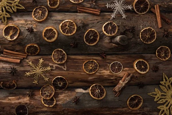 Vista dall'alto di fette di agrumi secchi con anice, bastoncini di cannella e fiocchi di neve decorativi su sfondo di legno — Foto stock
