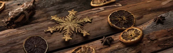 Rodajas de cítricos secos con anís, palitos de canela y copo de nieve decorativo sobre fondo de madera, plano panorámico - foto de stock