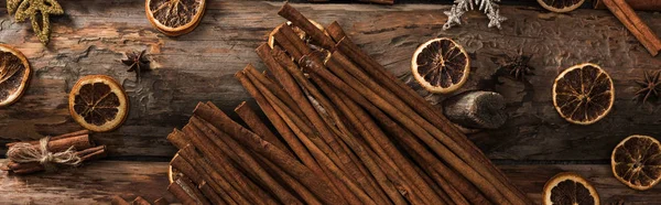 Top view of cinnamon sticks near anise, dried citrus slices and snowflakes on wooden background, panoramic shot — Stock Photo