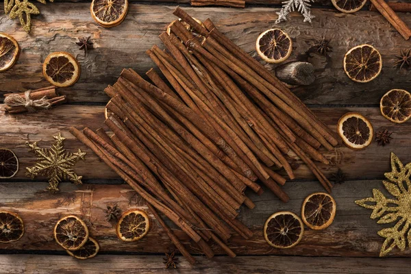 Vista superior de palitos de canela cerca de anís, rodajas de cítricos secos y copos de nieve sobre fondo de madera - foto de stock