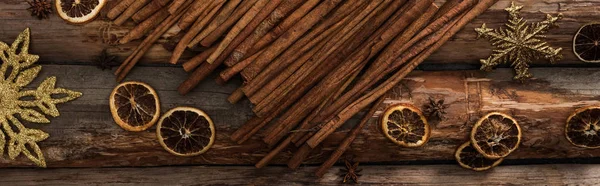 Вид сверху на коричные палочки рядом с анисом, сушеные цитрусовые ломтики и снежинки на деревянном фоне, панорамный снимок — стоковое фото