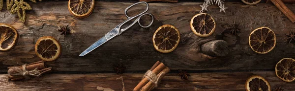Top view of cinnamon sticks, anise, dried citrus slices, scissors and snowflakes on wooden background, panoramic shot — Stock Photo